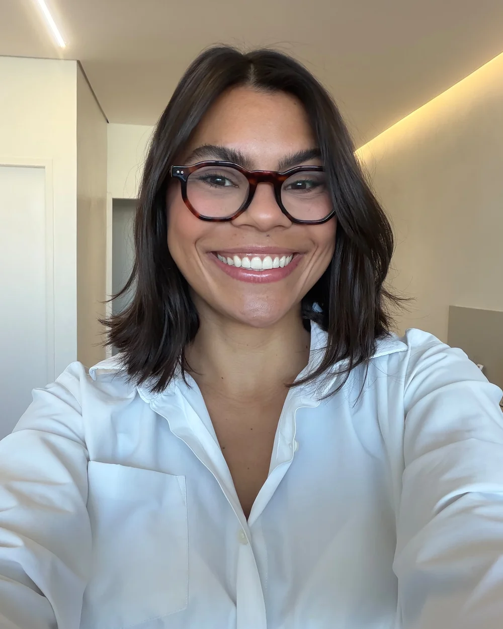 Camila Zolini Gimenez, sorrindo, de camisa branca e óculos